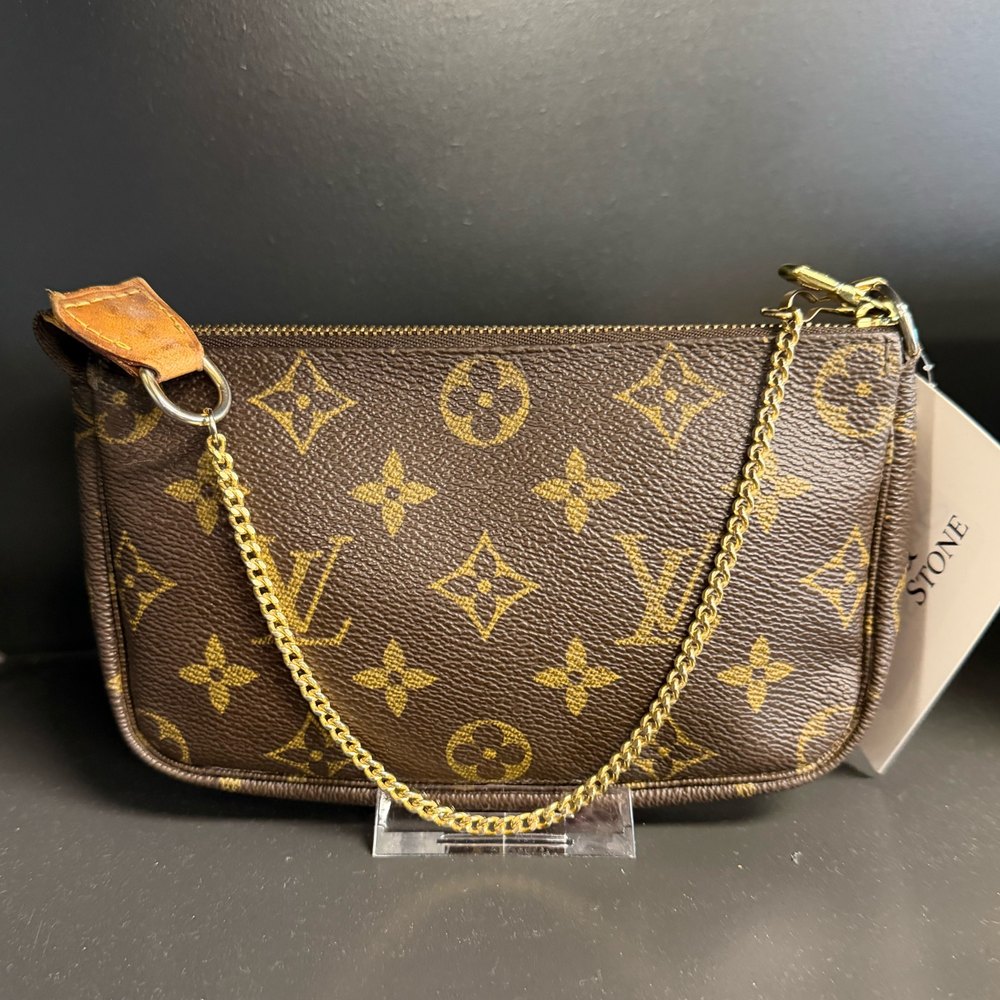 Louis Vuitton monogram canvas pochette with a gold chain strap, on a stand behind the counter at Silk & Stone